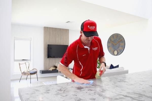ABOUT 2 AustClean professional cleaner in red uniform – domestic cleaning service provider cleaning marble countertops in modern Australian home using professional cleaning products and techniques.