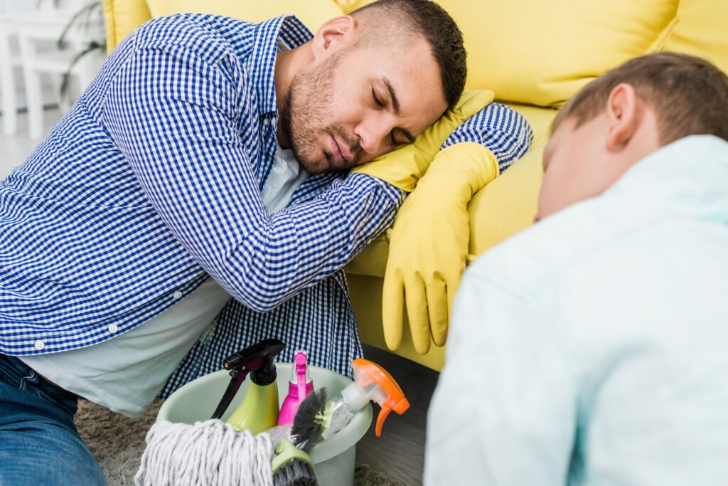 Exhausted cleaner in yellow gloves resting on couch after intensive cleaning session with mop and caddy nearby Mermaid Waters