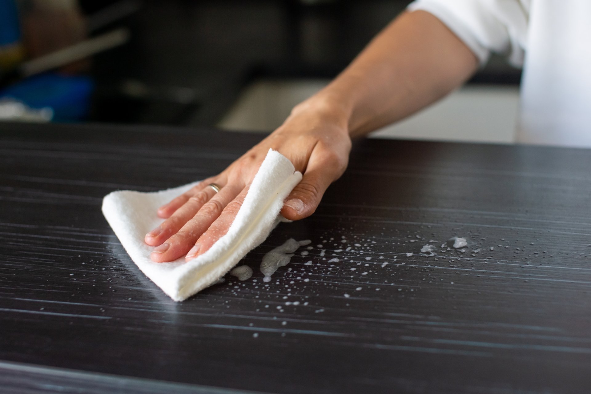 Fighting the Dust in South Australia: Pro Tips for a Cleaner Home 1 Hand wiping dark kitchen benchtop with white cloth removing soapy residue and water droplets
