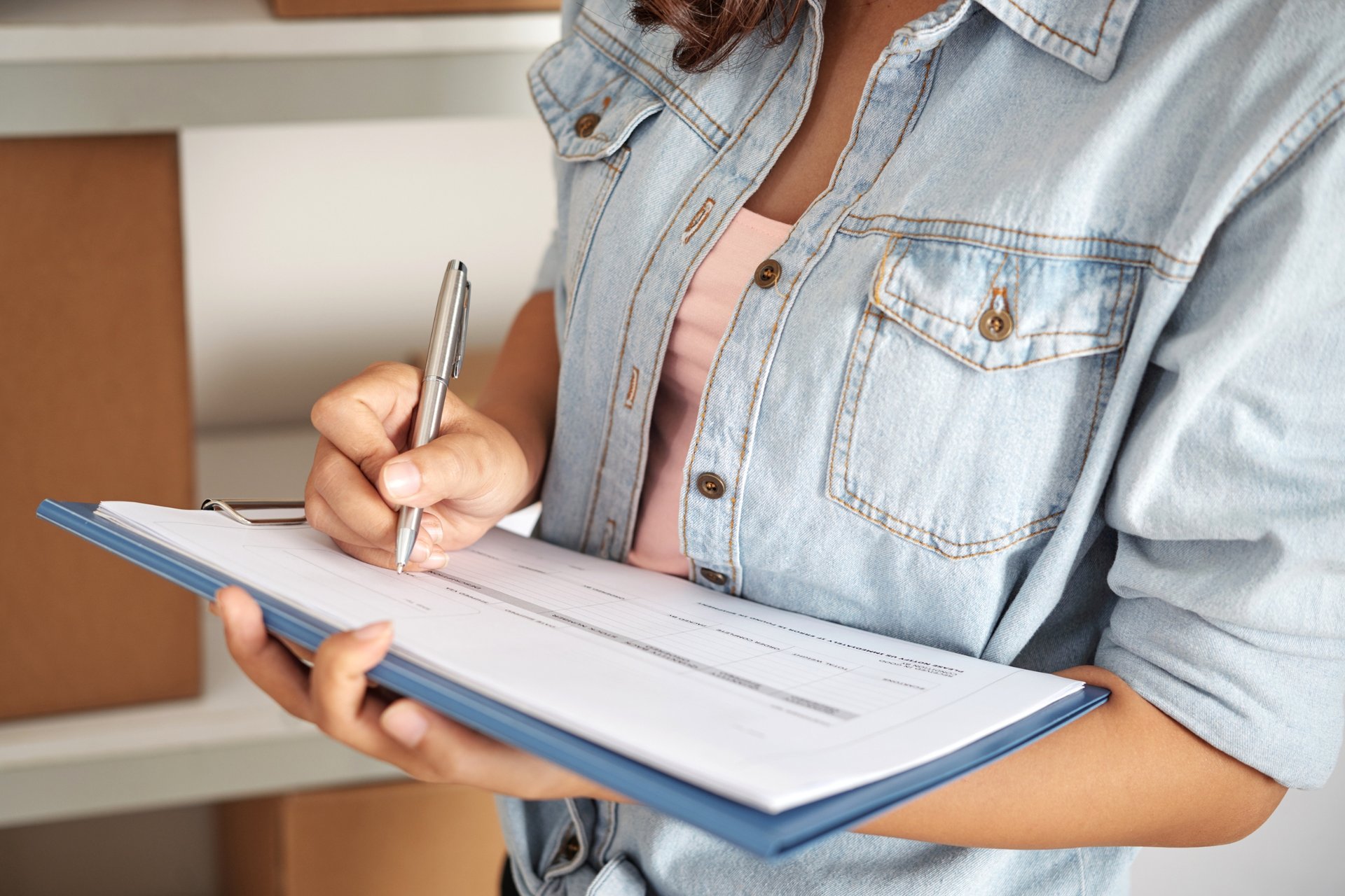 The Ultimate Bond Cleaning Checklist for Mermaid Waters Renters 1 Person in denim shirt writing on clipboard form with cardboard boxes visible on storage shelves behind inventory management