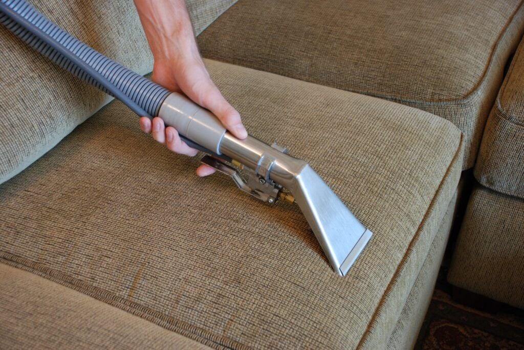 Interior Cleaning 1 AustClean professional upholstery cleaning in action – expert technician using specialized equipment to deep clean beige fabric sofa, demonstrating professional upholstery cleaning methods.